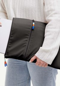 Funda negra acolchada para laptop con cremalleras dobles, acentos en azul, naranja y verde, sostenida con una mano. Parece ligera y duradera.