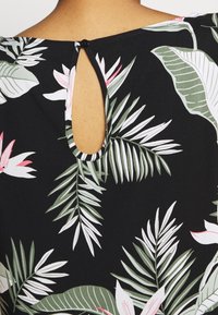 Tessuto nero con motivi di foglie tropicali bianche e verdi. Presenta un'apertura a occhio di chiave sul retro, fissata con un piccolo bottone nero.