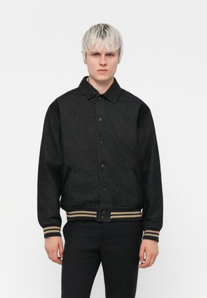 Black denim jacket with a button-up front, ribbed collar, and striped cuffs. Features two side pockets and a ribbed hem.