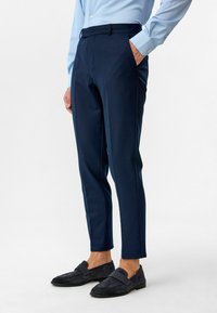 Marineblauwe broek met een getailleerde pasvorm, gemaakt van gladde stof. Heeft zijzakken en een nette tailleband, gecombineerd met donker suede instappers.