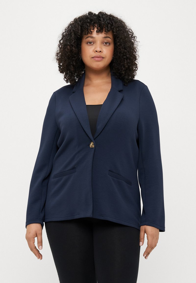 Blazer bleu marine en tissu doux, doté d'un bouton unique, de deux poches frontales et d'une coupe décontractée avec des manches longues.