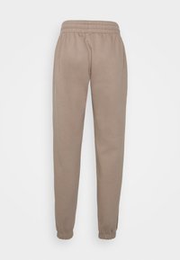 Světle hnědé tepláky vyrobené z měkkého materiálu, s elastickým pasem a tapered nohavicemi u kotníků. Hladká textura bez vzorů.