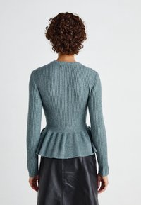 Pull en maille côtelée couleur sarcelle avec un corsage ajusté, un ourlet à basque et des manches longues, sur fond uni.