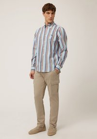 Gestreepte shirt in pastelkleuren met een button-down kraag, gecombineerd met beige cargobroeken en beige instappers, wat een casual outfit toont.