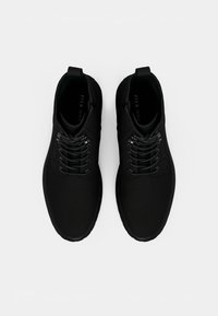 Černé tenisky s hladkým, matným povrchem, s krajkovým designem a smyčkovým poutkem na patě. Lehká gumová podrážka.