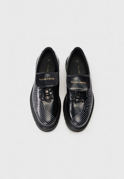 Chaussures en cuir noir avec des motifs de lignes blanches, dotées d'une languette rembourrée, de lacets ronds et d'une semelle texturée. Marquées "FILLING PIECES."