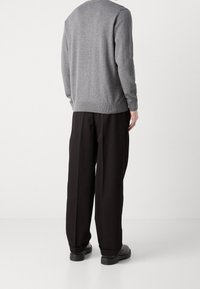 Maglione grigio di lana con maniche lunghe, polsini e orlo a coste, abbinato a pantaloni neri a gamba larga e scarpe nere. Linee semplici e pulite.