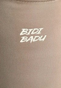Tessuto ribbed marrone chiaro con la scritta "BIDI BADU" in un carattere bold, bianco, stile graffiti.