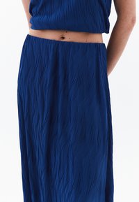 Vloeiende blauwe twee-delige outfit van textuurstof, met een golvend patroon en een elastische tailleband, met een top die de buik onthult.