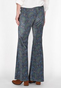 Uitlopende broeken van een soepele stof, met een blauw en groen paisleypatroon en bruine blokhakken zichtbaar eronder.