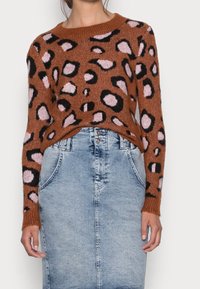 Brązowy sweter z czarnymi i różowymi cętkami w stylu lamparta, zestawiony z jasnoniebieską spódnicą dżinsową z dwoma przednimi kieszeniami i guzikiem w pasie.