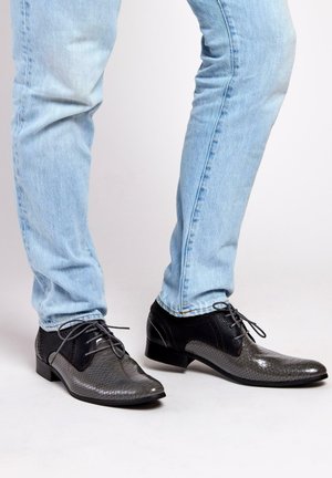 Zwarte en grijze veterschoenen met een gestructureerd, patroonoppervlak. Gladde neus en gaasaccenten. Gecombineerd met lichtblauwe spijkerbroeken.