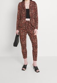 Blazer och byxor med blommönster i nyanser av röd och brun, tillverkade av texturerad tyg. Kombinerat med svarta öppna klackskor.