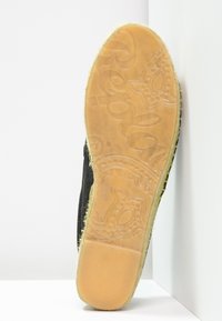 Zapato negro con un upper texturizado, que presenta una suela de goma en tono miel con intrincados patrones en relieve. El lado muestra detalles suaves y costuras.