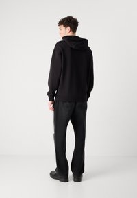 Schwarzer Kapuzenpullover mit Kängurutasche, aus weichem Stoff. Kombiniert mit dunklen Jeans und schwarzen Schuhen, zeigt er eine lässige Silhouette.