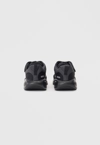 Chaussures de sport noires avec tige en maille, talon texturé et semelle arrondie. Elles disposent d'une languette de tirage et d'une finition lisse. Design minimaliste sans logos visibles.