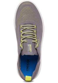 Zapatilla deportiva gris con un empeine de malla, acentos amarillos y detalles reflectantes. Presenta una plantilla azul acolchada y una suela de goma blanca.