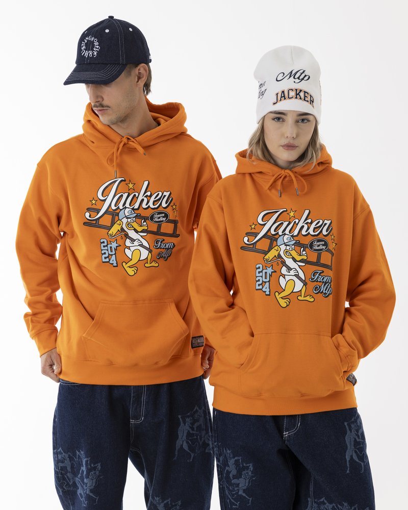 Orange hoodies with graphic prints, featuring cartoon-style characters. One model wears a white beanie, the other a dark cap. Blue jeans displayed.