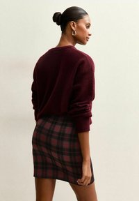 Burgundy knit sweater with long sleeves paired with a black and red plaid mini skirt. Smooth texture and fitted design.
