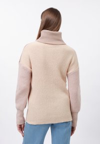 Oversized gebreide trui met een hoge kraag, geribbelde textuur en een kleurblokkende ontwerp in lichtbeige en zachtroze.