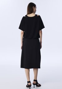 Zwarte oversized t-shirt met korte mouwen, met een open schouderontwerp. Gecombineerd met een bijpassende zwarte rok, met een soepele textuur en een slim fit.