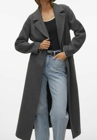 Lang grå uldblandingsfrakke med notched krave, afslappet pasform og sidelommer, båret over en sort top og løse lyseblå jeans.