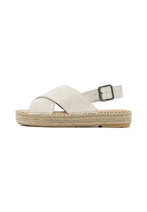 Beige suède sandalen met kruislings gespen, een gewaxt jute zool en een verstelbare metalen gesp op de enkelriem.