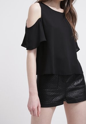 Schwarzes Cold-Shoulder-Oberteil mit ausgestellten Ärmeln aus weichem Stoff. Kombiniert mit strukturierten schwarzen Shorts mit Steppmuster.