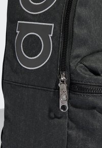 Črni nahrbtnik iz blaga s poudarjeno logotipom, zapiranjem na zadrgo s srebrno kovino in teksturirano površino.