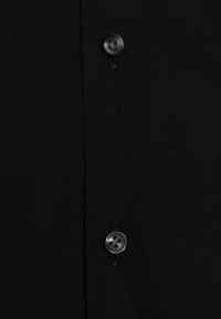 Tela de camisa negra con una fila de botones negros. El material parece suave con un ligero brillo y una textura mínima visible.