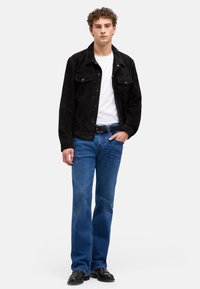 Czarna zamszowa kurtka noszona na białej koszulce, zestawiona z niebieskimi dżinsami z rozszerzanymi nogawkami i czarnymi butami. Posiada dwie kieszenie na piersi i kołnierzyk.