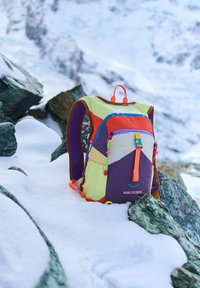 Multicolored backpack with sections in orange, purple, yellow, and cream. Features a front pocket, shoulder straps, and decorative hardware.