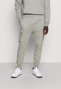 Grå bomullsjoggers med en avslappnad passform, med sidofickor, ribbade muddar och en Nike-logotyp på vänstra fickan. Bärs med vita sneakers.