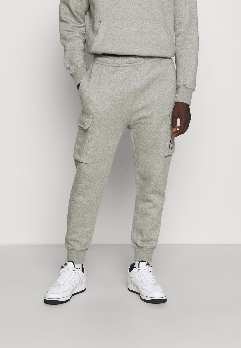Grå bomullsjoggers med en avslappnad passform, med sidofickor, ribbade muddar och en Nike-logotyp på vänstra fickan. Bärs med vita sneakers.