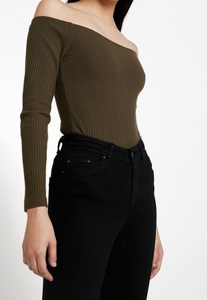 Kvinde iført en olivengrøn, off-shoulder ribbet langærmet top kombineret med højtaljede sorte jeans.