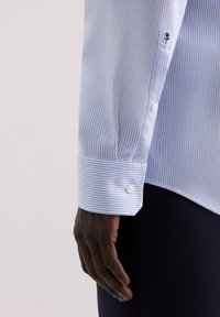 Lichtblauwe overhemd met een subtiel gestreept patroon, knoopmanchetten en zachte katoenen stof. Inclusief een klein geborduurd detail op de mouw.