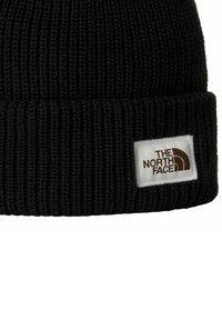 Beanie nera lavorata a maglia con una consistenza a costine spesse. Presenta una toppa bianca con il logo "THE NORTH FACE" e un design ad arco marrone.
