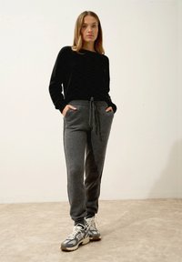 Šedé teplákové kalhoty s šňůrkou v pase a bočními kapsami, doplněné černým svetr s dlouhými rukávy a šedými sportovními botami.