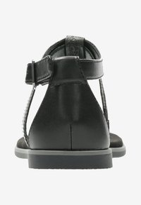 Sandali neri in pelle con cinturino posteriore, suola piatta e fibbia regolabile. Il design presenta una banda texturizzata e accessori minimi.
