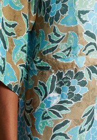 Korte mouwen stof met een bloemenontwerp in blauwe, groene en bruine kleuren. Getextureerd met stippen en zichtbare naaddetails.