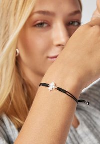 Pulsera tejida negra con un encanto de estrella de mar blanca y un pequeño acento de perla, asegurada con cordones ajustables y extremos de plata.