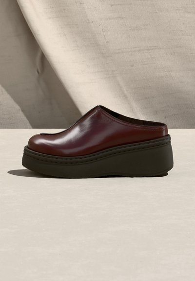 Ενιαίο καφέ σκούρο δερμάτινο παπούτσι κλογκ με παχύ μαύρο πάτο πλατφόρμα σε ανοιχτή επιφάνεια με φόντο από βρεγμένο ύφασμα.