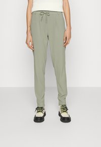 Calças de treino verde claro com cintura elástica ajustável, design ajustado e textura suave. Combinadas com ténis robustos e de várias cores.