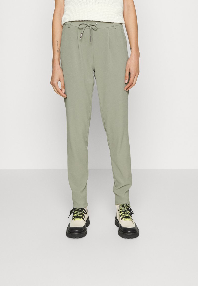 Calças de treino verde claro com cintura elástica ajustável, design ajustado e textura suave. Combinadas com ténis robustos e de várias cores.