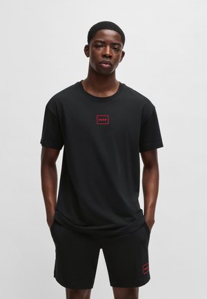 T-shirt en coton noir avec un logo rectangulaire rouge portant le mot "HUGO" sur la poitrine. Associé à un short noir avec une patch logo assortie.