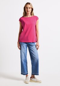 Top corto fucsia de manga corta combinado con jeans de pierna ancha azul claro. Los jeans tienen dobladillos deshilachados y se complementan con zapatillas deportivas blancas.
