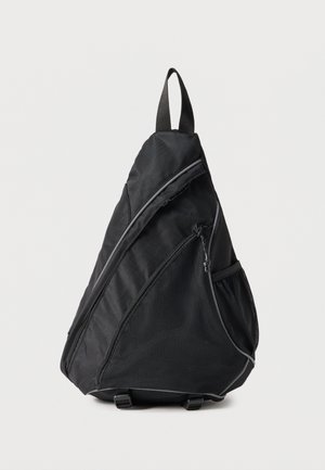 Mochila bandolera triangular negra con bolsillo delantero con cremallera, bolsillo lateral de malla y asa superior para llevar, sobre un fondo liso.