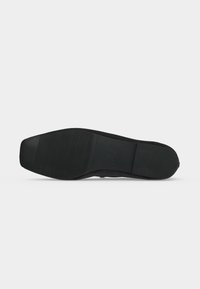 Semelle de chaussure formelle noire avec des zones de grip texturées sur l’avant, le milieu et le talon sur fond clair uni.