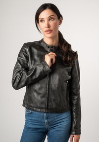 Schwarze Lederjacke mit einem figurbetonten Design, einem hohen Kragen, einem Frontreißverschluss und subtiler Textur. Kombiniert mit blauen Jeans.