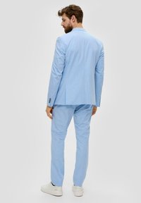 Lichtblauw kostuum met een getailleerde blazer en rechte pijpen, gemaakt van textuurstof. Kenmerkt zich door een notch lapel en knoopmanchetten.